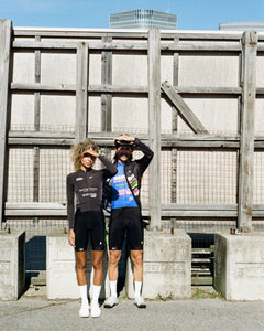 Racing Dream Team members Niara and Phil shield their eyes from the sun, wearing the latest collection in mostly black with a pop of blue and graphics