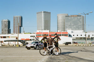 Racing Dream Team Director Coco with Niara and Agatha holding the Specialized Aethos in front of the FAT 911 Dakar team car. Landscape shot with lots of sunlight, featuring FAT cap