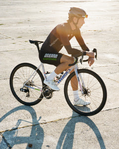 Racing Dream Team member Michi on break from efforts at training camp, contemplates things. Concrete background glowing from sunshine. Featuring the team-issue Specialized Aethos bike in moongem color way and latest collection. Dream Beyond!