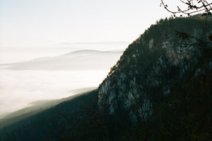 A scenic view, the silhouette of a mountaintop fills half the frame while sun spills into the valley below.