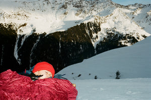 Tighter crop on a snowy mountain summit, in the corner a child bundled in striking red.