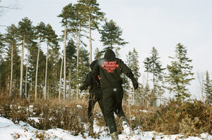 Two figures running into a winter forest while wearing TSOT sweaters.